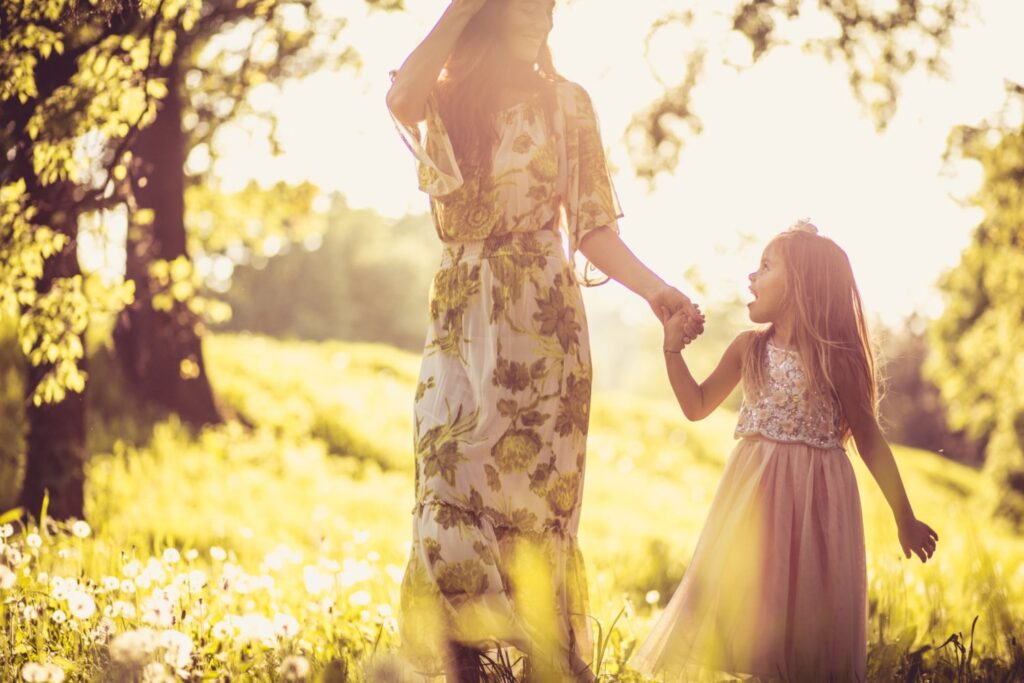 Get outside for at least 20 minutes each day - Woman and young girl in dresses holding hands in meadow