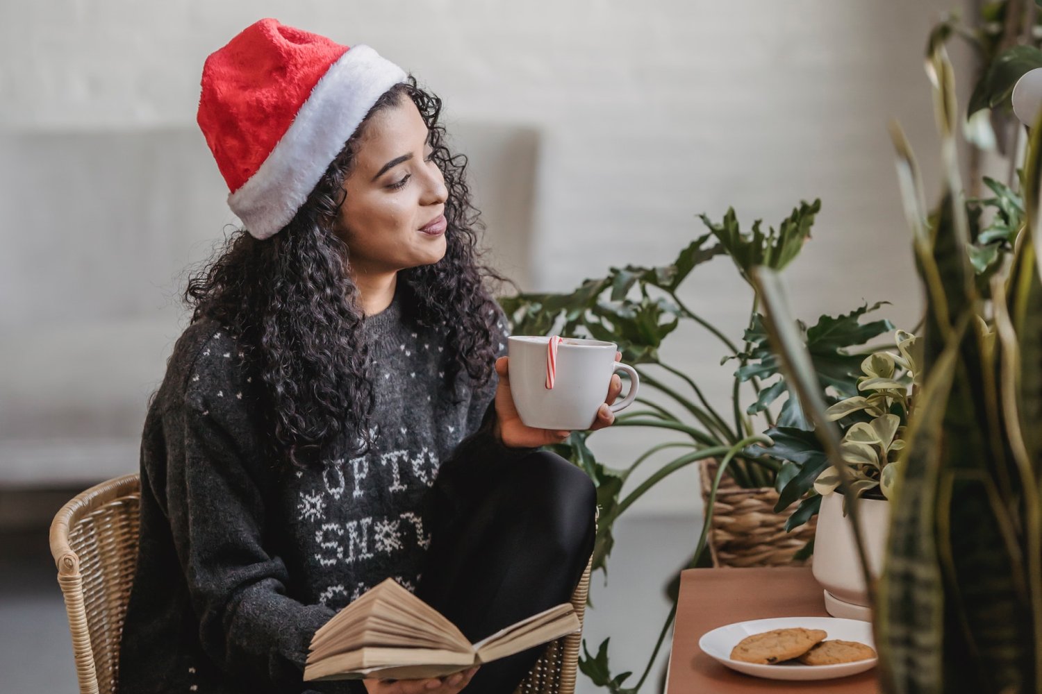 How to stay calm and peaceful during Christmas - Woman sitting at table with Christmas hat cup and book