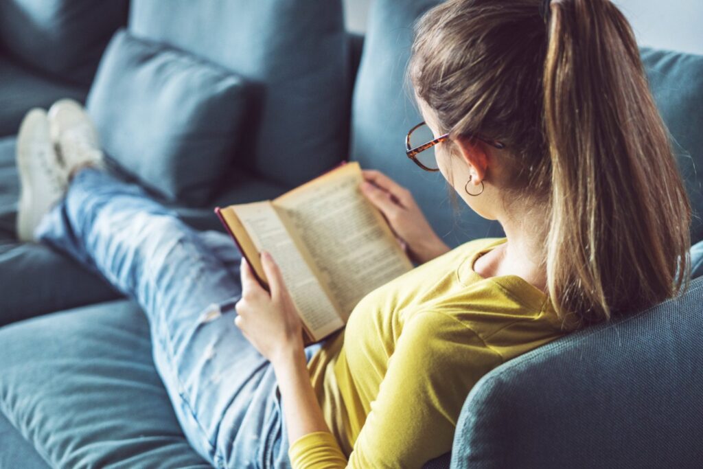 Read an inspiring book or blog post - Woman reading book relaxing in couch