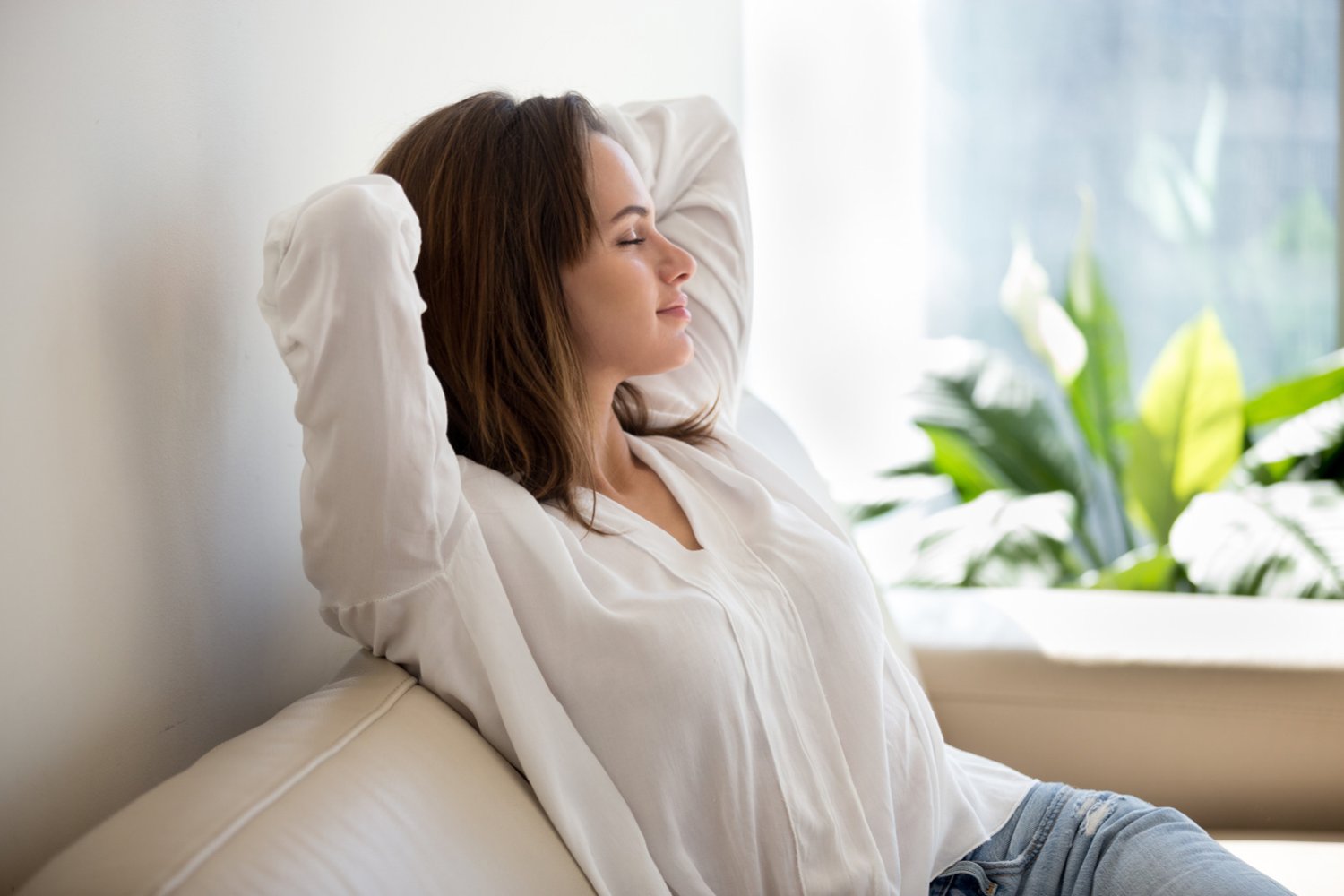 How mindfulness helps - Smiling woman sitting in couch with eyes closed hands behind head