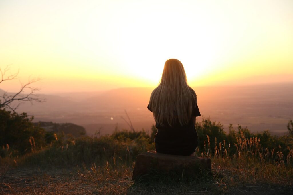 Mindfulness - Peaceful woman sitting in nature looking at sunset