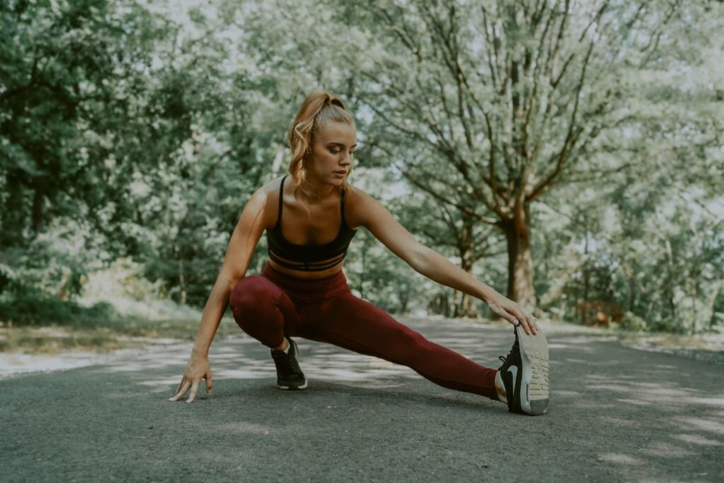 Physical health - Woman in training outfit stretching on path under trees