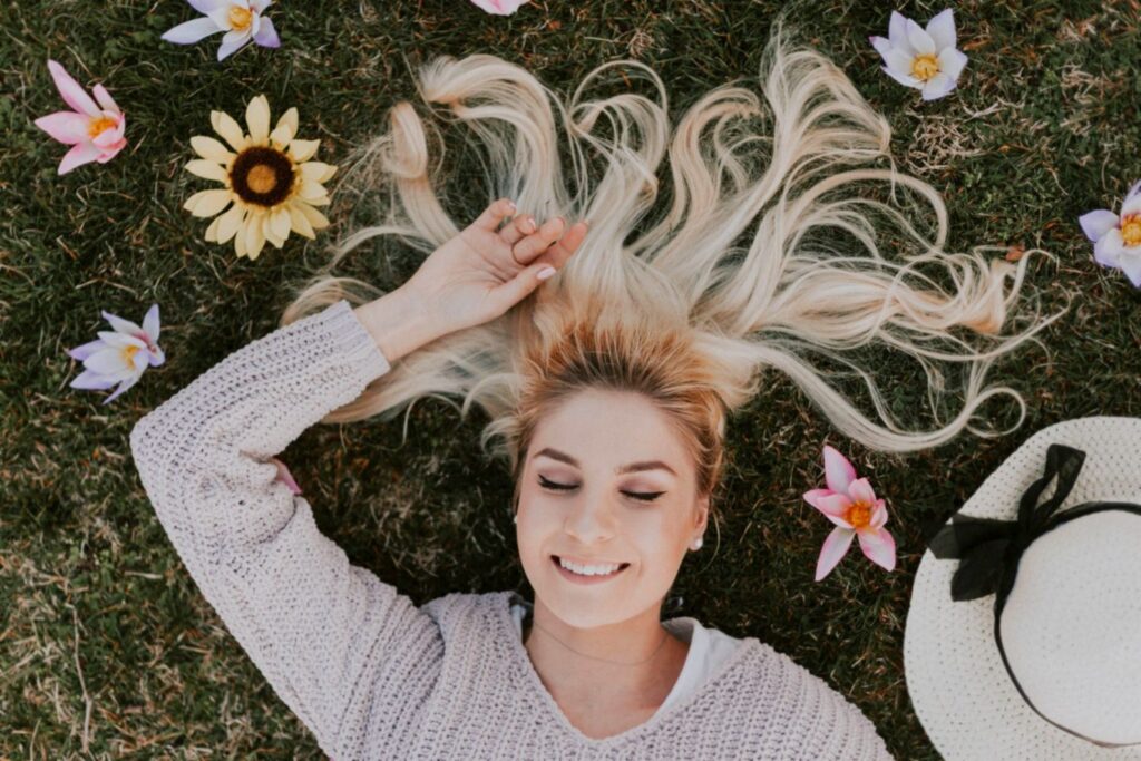 Emotional well-being when mindful - Smiling woman eyes closed lying on grass with flowers