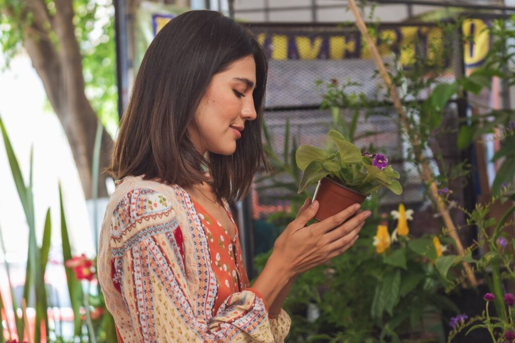 How to become more mindful - Woman in front of plants and flowers looking at plant in hands