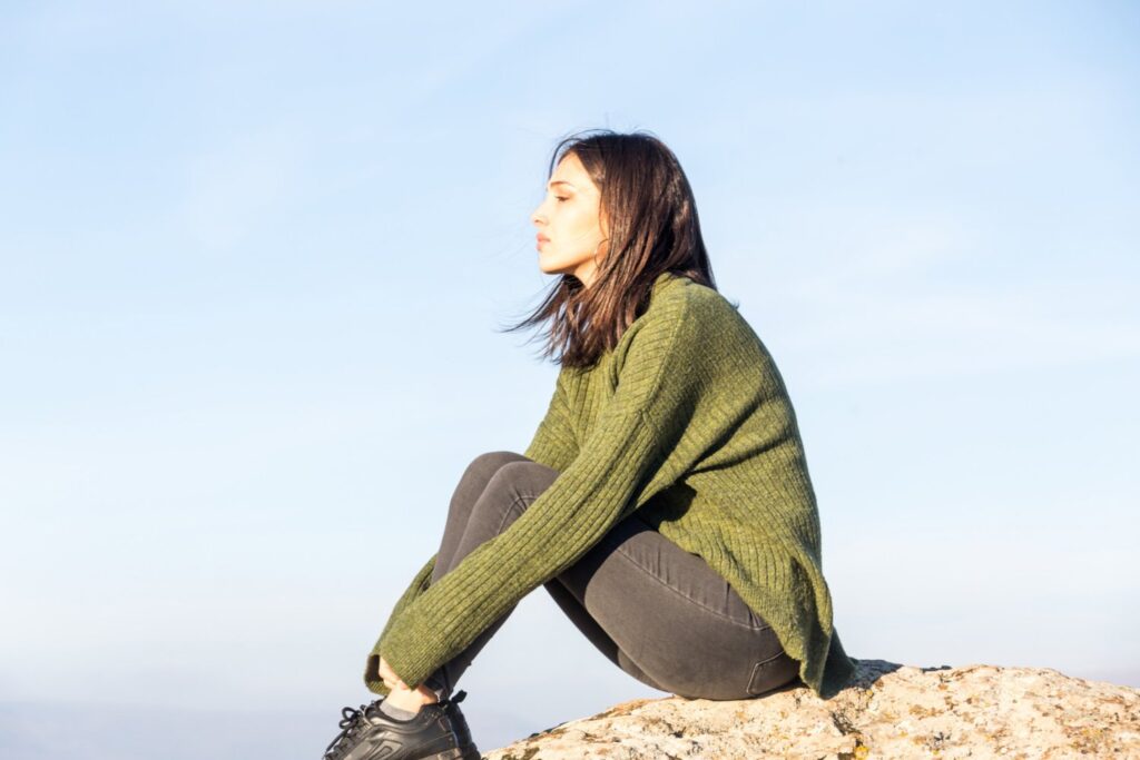 Tips for staying mindful when things get tough - Woman sitting outside on rock